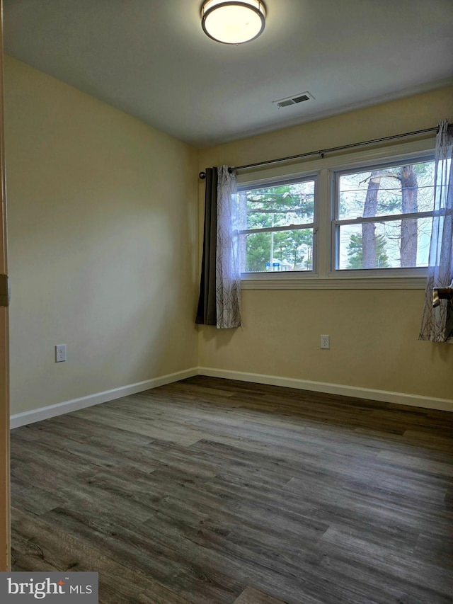 empty room featuring dark wood-type flooring, baseboards, and visible vents