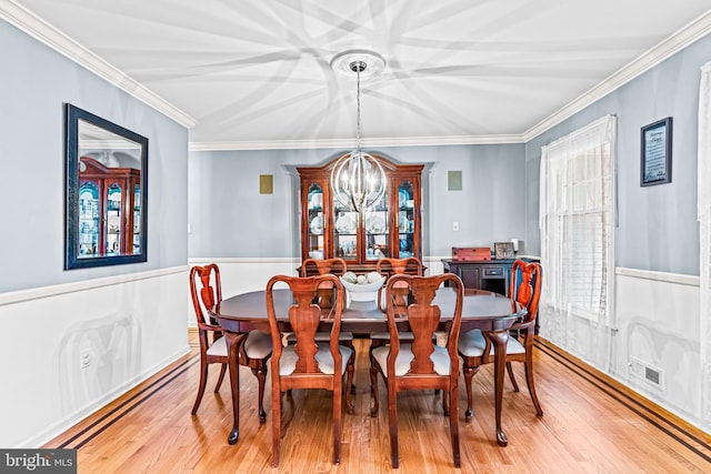 dining space with a chandelier, light wood finished floors, visible vents, and crown molding