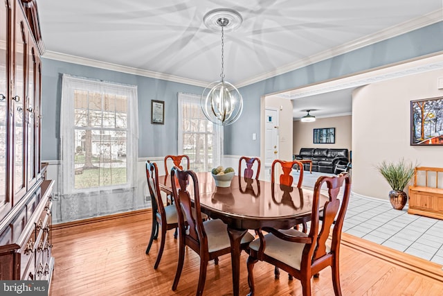 dining room with crown molding, a notable chandelier, wainscoting, and light wood-type flooring