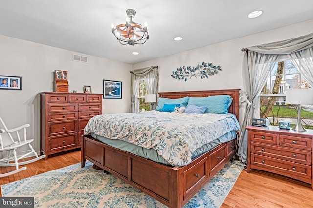 bedroom featuring light wood finished floors, an inviting chandelier, multiple windows, and visible vents