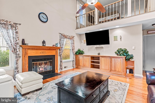 living room featuring a fireplace with flush hearth, light wood finished floors, a towering ceiling, and plenty of natural light