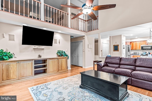 living area with baseboards, light wood-type flooring, a towering ceiling, and a ceiling fan