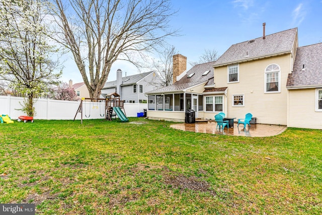 rear view of house with a chimney, a patio area, a fenced backyard, a sunroom, and a playground