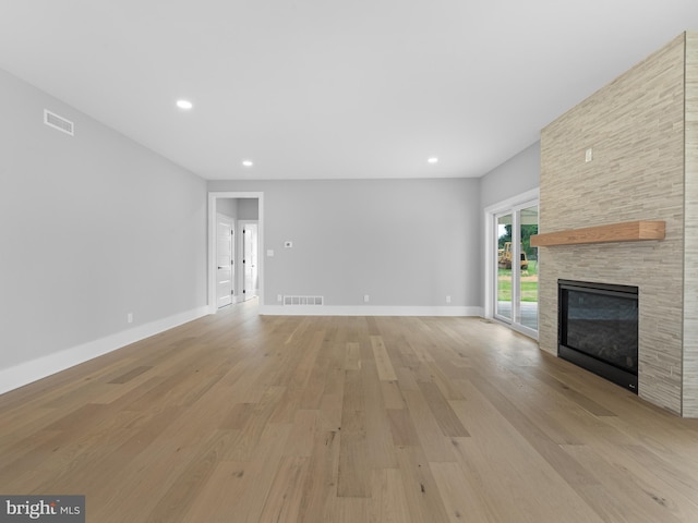 unfurnished living room with light wood-type flooring, a fireplace, baseboards, and visible vents