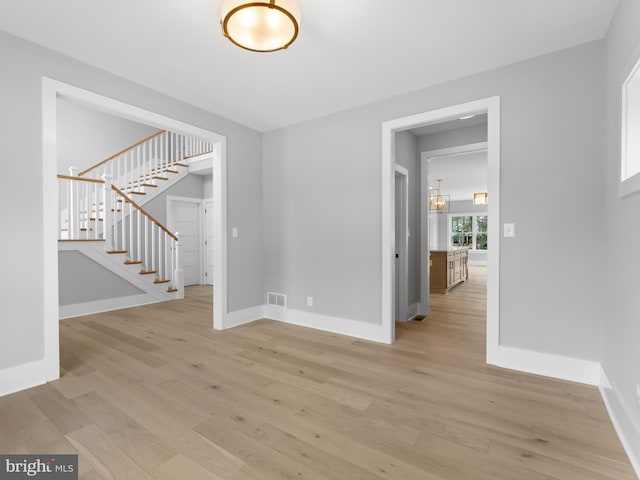 empty room with stairway, visible vents, baseboards, and light wood-style flooring