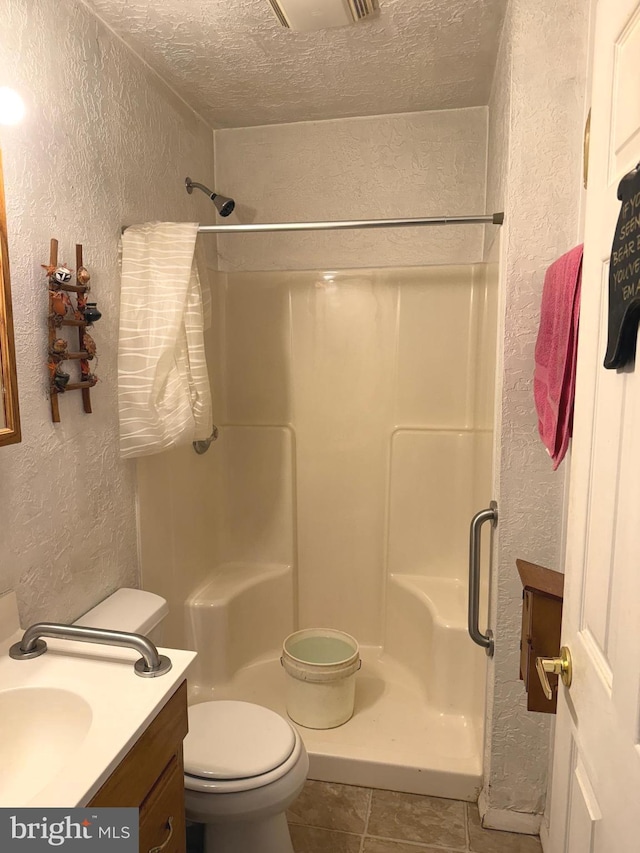full bathroom with tile patterned floors, a textured wall, a stall shower, and toilet