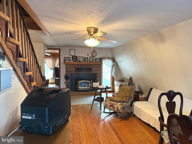 living area with wood-type flooring, a brick fireplace, ceiling fan, stairway, and a textured ceiling