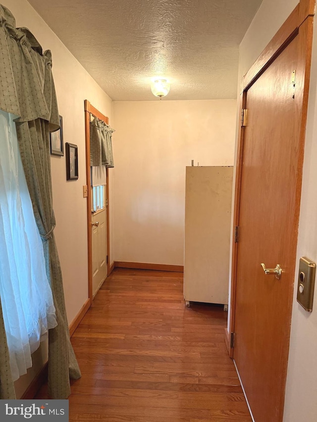 hallway featuring baseboards, a textured ceiling, and wood finished floors