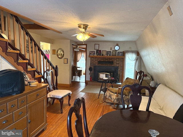 living area with a ceiling fan, a fireplace, stairway, baseboards, and light wood-style floors