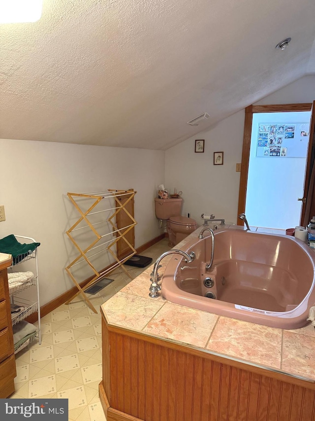 full bathroom featuring a textured ceiling, tile patterned floors, baseboards, a tub with jets, and vaulted ceiling