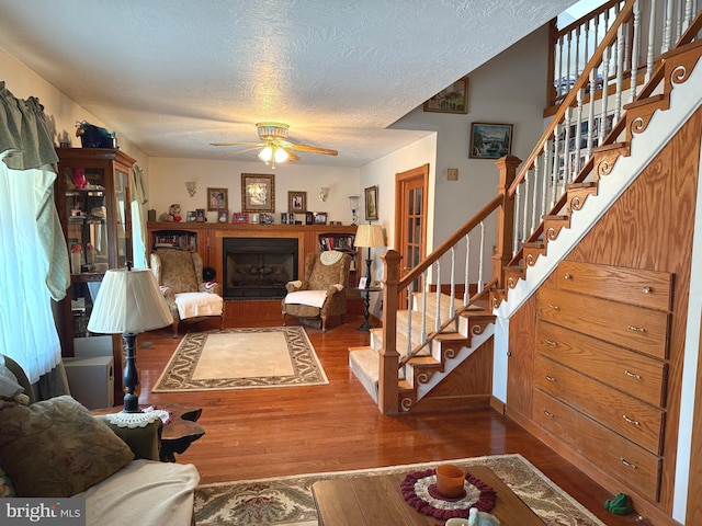 living room featuring a ceiling fan, a textured ceiling, a fireplace, wood finished floors, and stairs