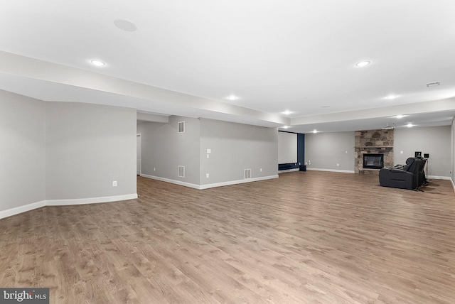 finished basement featuring light wood-style floors, baseboards, recessed lighting, and a stone fireplace