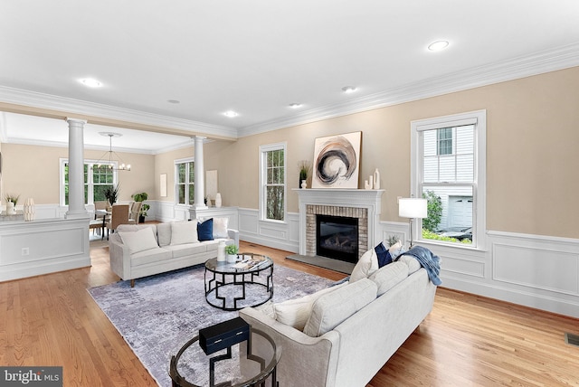 living room with crown molding, a fireplace, ornate columns, and wood finished floors