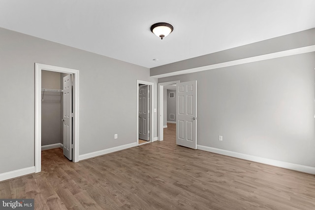 unfurnished bedroom with baseboards, wood finished floors, and a walk in closet