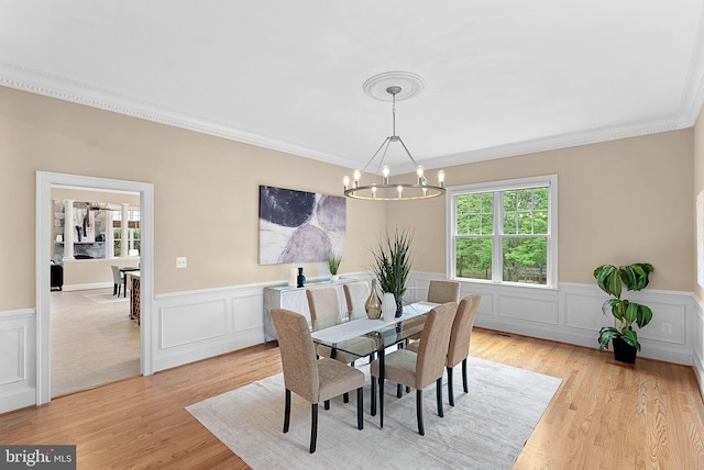 dining area with an inviting chandelier, ornamental molding, a wainscoted wall, and a wealth of natural light