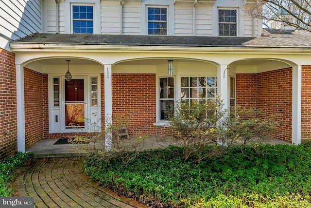 view of exterior entry featuring brick siding and covered porch