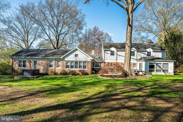 back of house with a hot tub, a chimney, a lawn, and brick siding