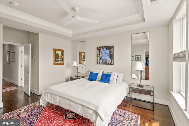 bedroom featuring ceiling fan, a tray ceiling, baseboards, dark wood-type flooring, and visible vents