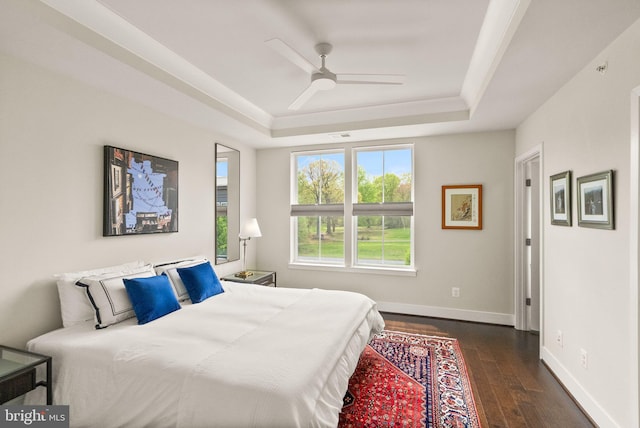 bedroom featuring baseboards, a tray ceiling, ceiling fan, and dark wood finished floors