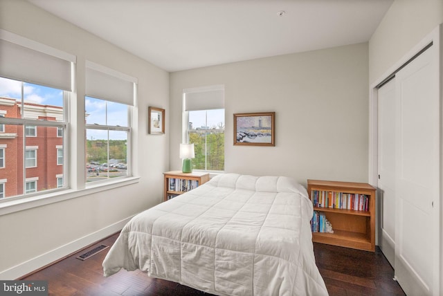 bedroom with a closet, wood finished floors, visible vents, and baseboards