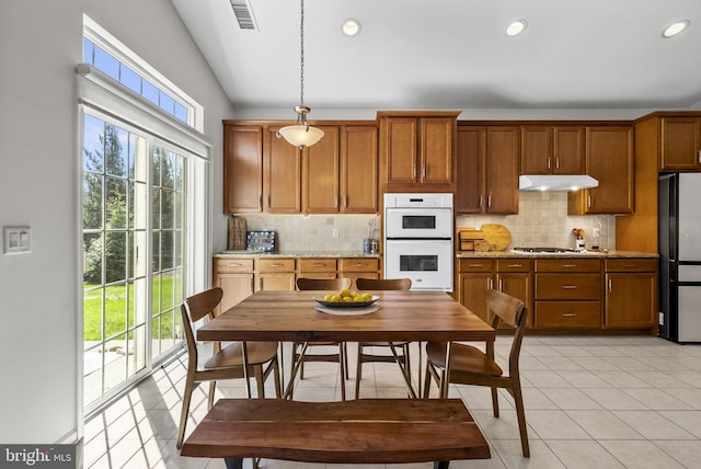kitchen with freestanding refrigerator, white double oven, brown cabinetry, visible vents, and under cabinet range hood