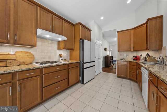kitchen with white appliances, vaulted ceiling, under cabinet range hood, light tile patterned flooring, and a sink