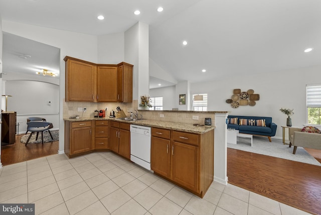 kitchen featuring light tile patterned floors, a peninsula, brown cabinets, white dishwasher, and a sink