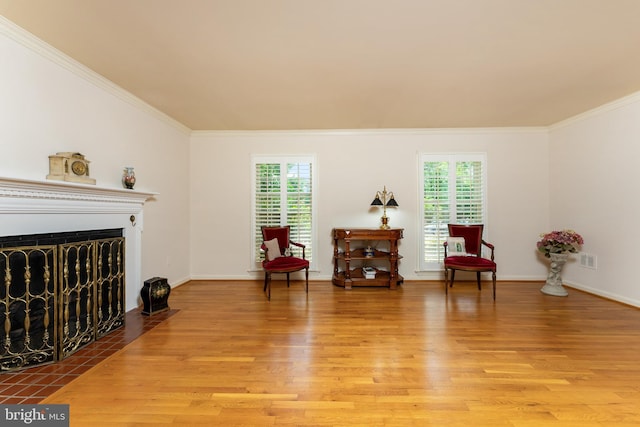 sitting room with plenty of natural light, wood finished floors, crown molding, and a fireplace with flush hearth