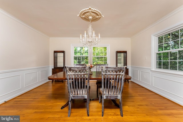 dining room with a chandelier, ornamental molding, light wood finished floors, wainscoting, and a decorative wall
