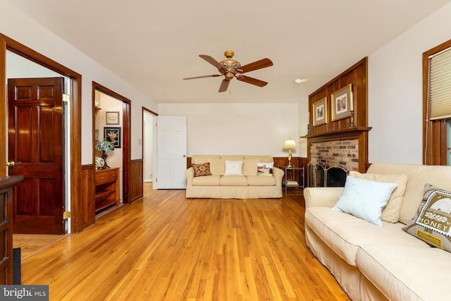 living room featuring a ceiling fan, light wood-style floors, and a brick fireplace