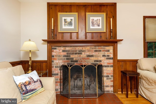 living room featuring wainscoting, wood walls, and a brick fireplace