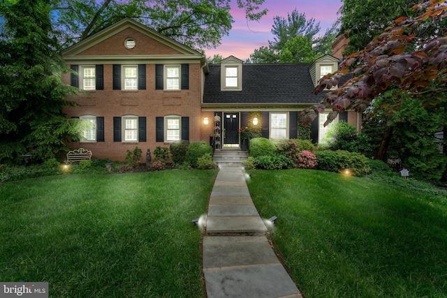 colonial inspired home with a yard, brick siding, and a shingled roof
