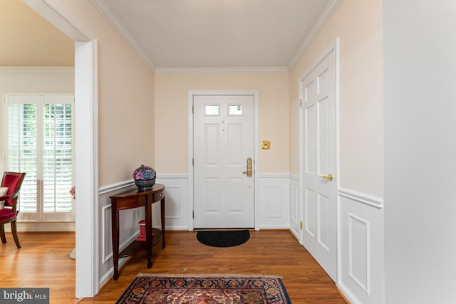 foyer featuring ornamental molding, wood finished floors, a wainscoted wall, and a decorative wall