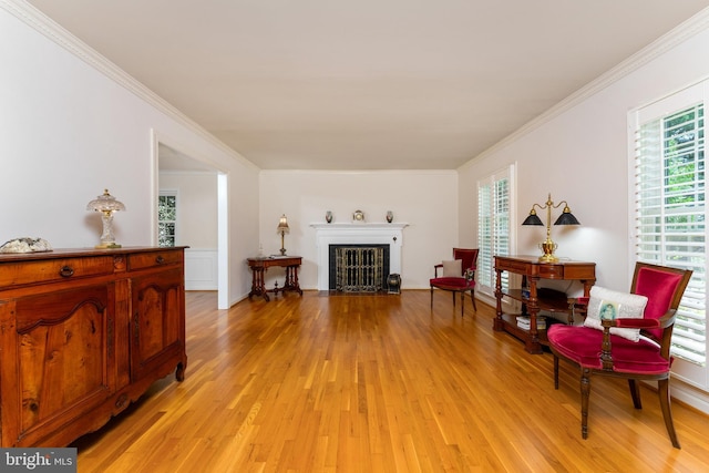 sitting room with light wood finished floors, crown molding, and a fireplace with flush hearth
