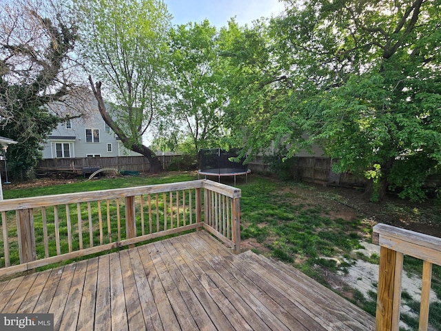 wooden deck featuring a trampoline, a fenced backyard, and a lawn