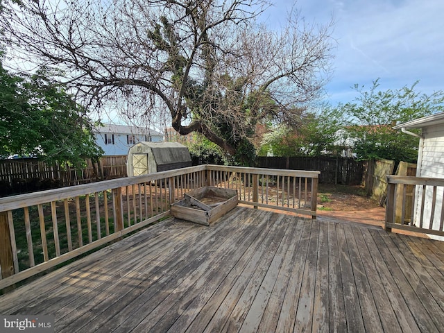 wooden deck featuring a storage shed, an outbuilding, and a fenced backyard