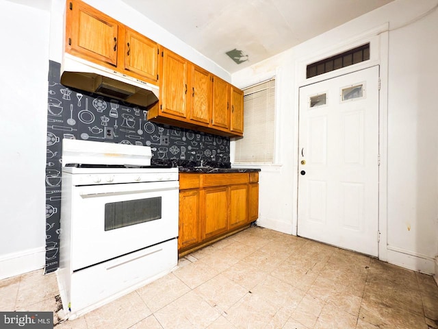 kitchen featuring under cabinet range hood, brown cabinets, baseboards, and white gas range oven