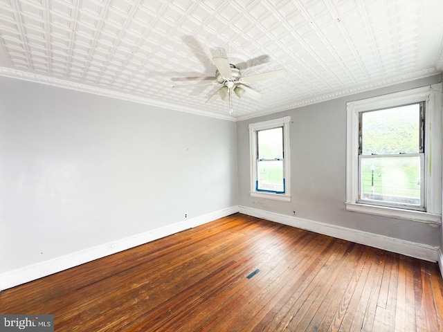 spare room with ornamental molding, a ceiling fan, visible vents, baseboards, and hardwood / wood-style flooring