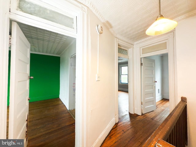 hallway featuring baseboards, wood-type flooring, ornamental molding, and an ornate ceiling