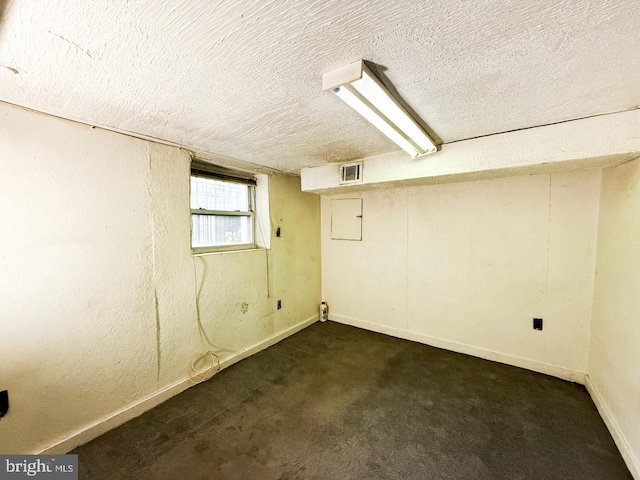 below grade area with baseboards, visible vents, a textured ceiling, and dark carpet