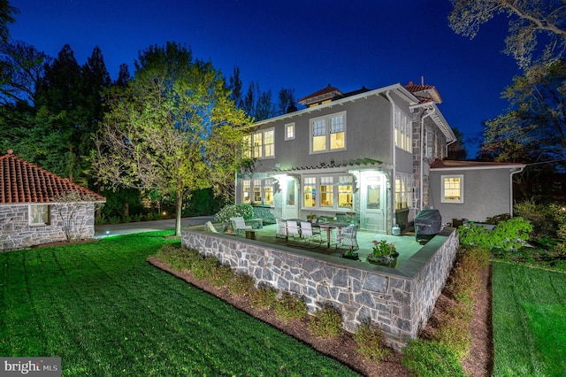 3712 Bradley Ln, Chevy Chase, MD 20815 - back of house at night featuring stucco siding, a patio area, and a yard