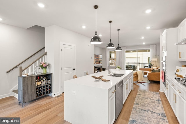 kitchen with a sink, stainless steel dishwasher, light wood-style floors, and white cabinets