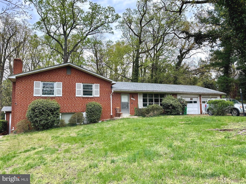 tri-level home with brick siding, a front lawn, a chimney, and an attached garage