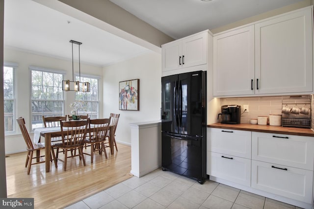 kitchen with white cabinetry, ornamental molding, freestanding refrigerator, and butcher block counters