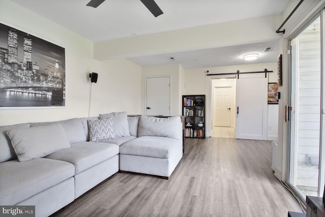 living area with a ceiling fan, visible vents, a barn door, wood finished floors, and baseboards