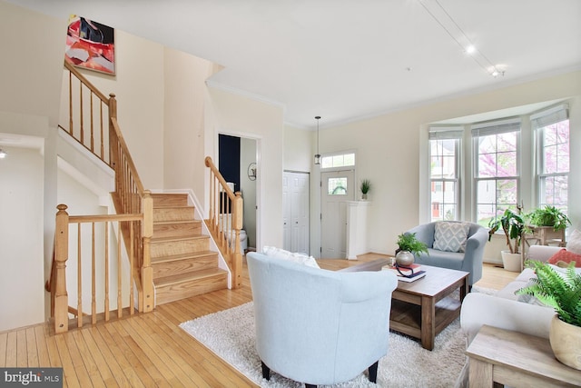 living room featuring light wood-type flooring, crown molding, and stairs