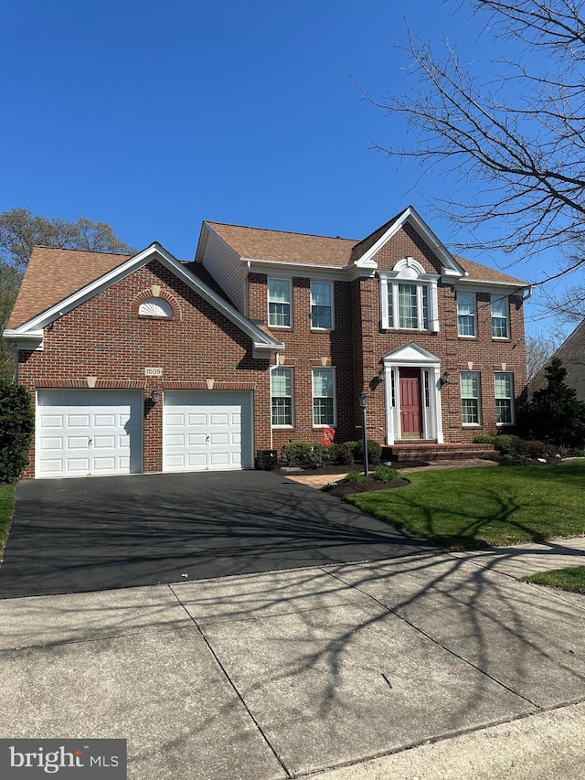 colonial inspired home featuring brick siding, aphalt driveway, and a garage