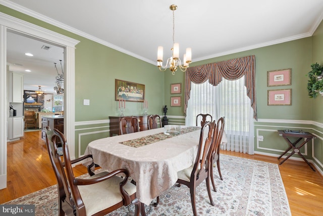 dining area with light wood-style flooring, a notable chandelier, and crown molding