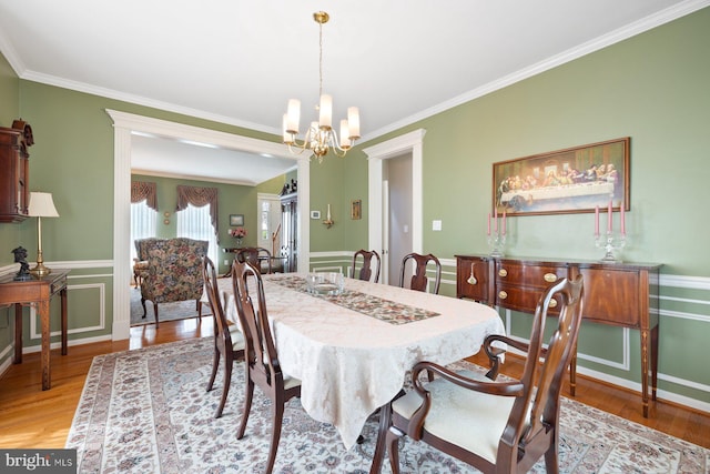 dining space featuring wainscoting, a notable chandelier, crown molding, and light wood finished floors