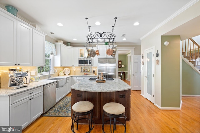 kitchen with stainless steel appliances, a kitchen island, crown molding, decorative backsplash, and light wood-style flooring